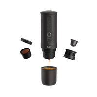 Outin Nano portable espresso machine in Space Grey with ground coffee, coffee capsules and a glass of espresso