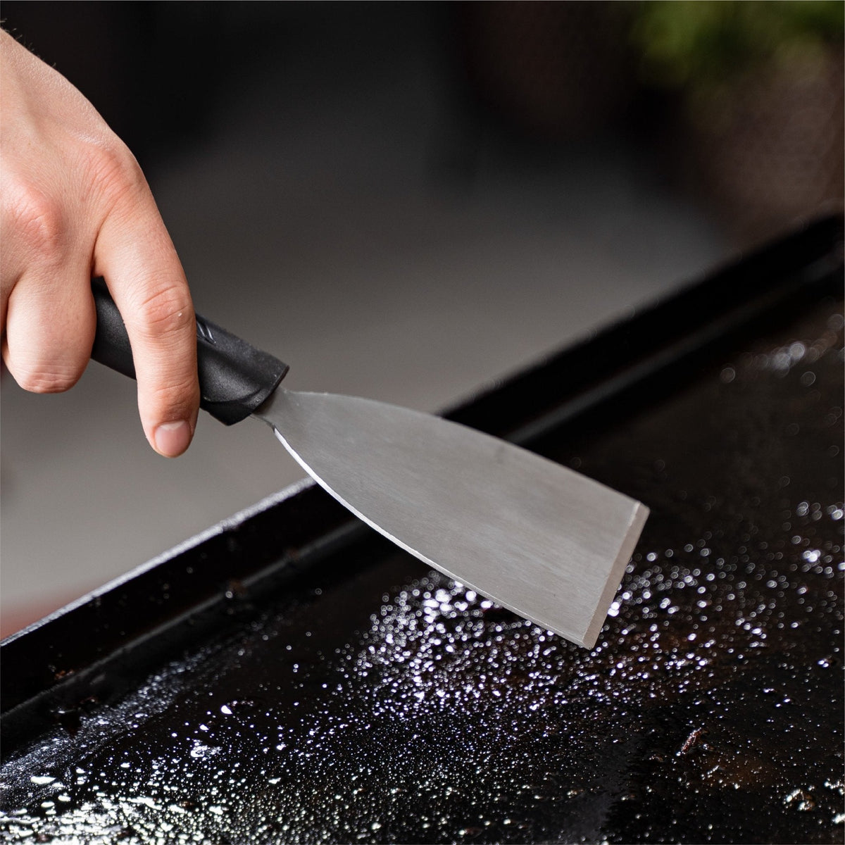 Blackstone 8 Piece Griddle Cleaning Kit - scraping debris from the plate
