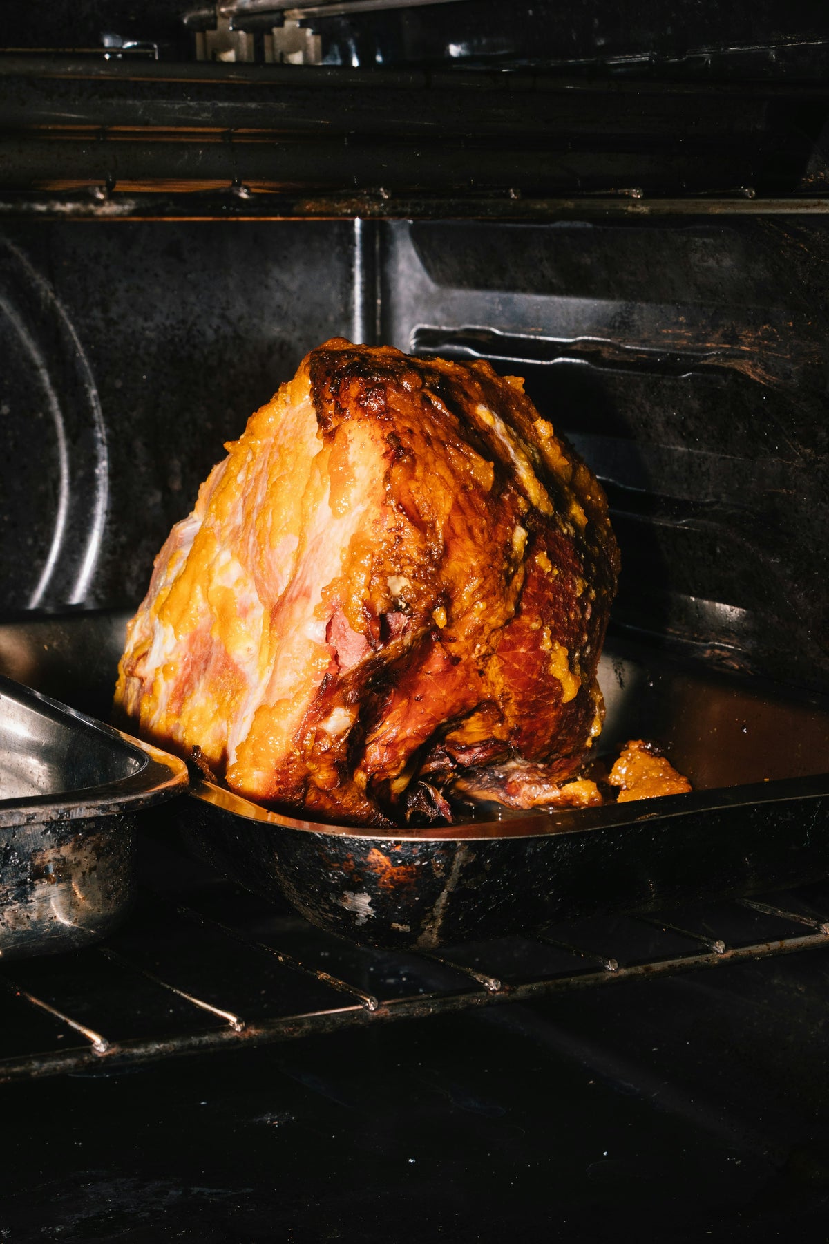 Glazed ham roasting in a tray inside a dark oven