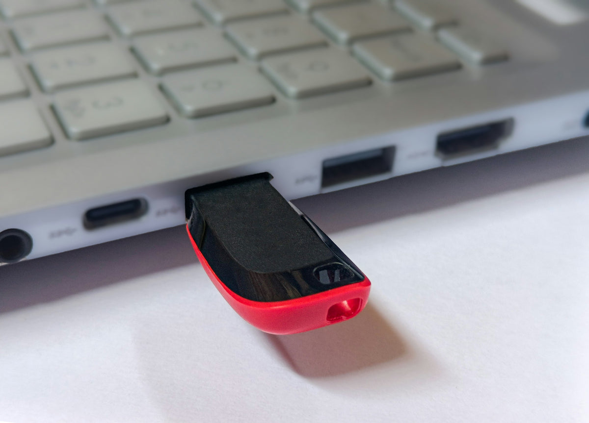 A red and black USB memory stick plugged into the side of a silver laptop