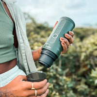 Outin Nano portable espresso machine in Forest Green with ground coffee, coffee capsules and a glass of espresso