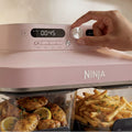 Ninja Crispi DualZone Glass Air Fryer in Rose Quartz, close-up of hand pouring milk into the tumbler-style dial area on a pink unit
