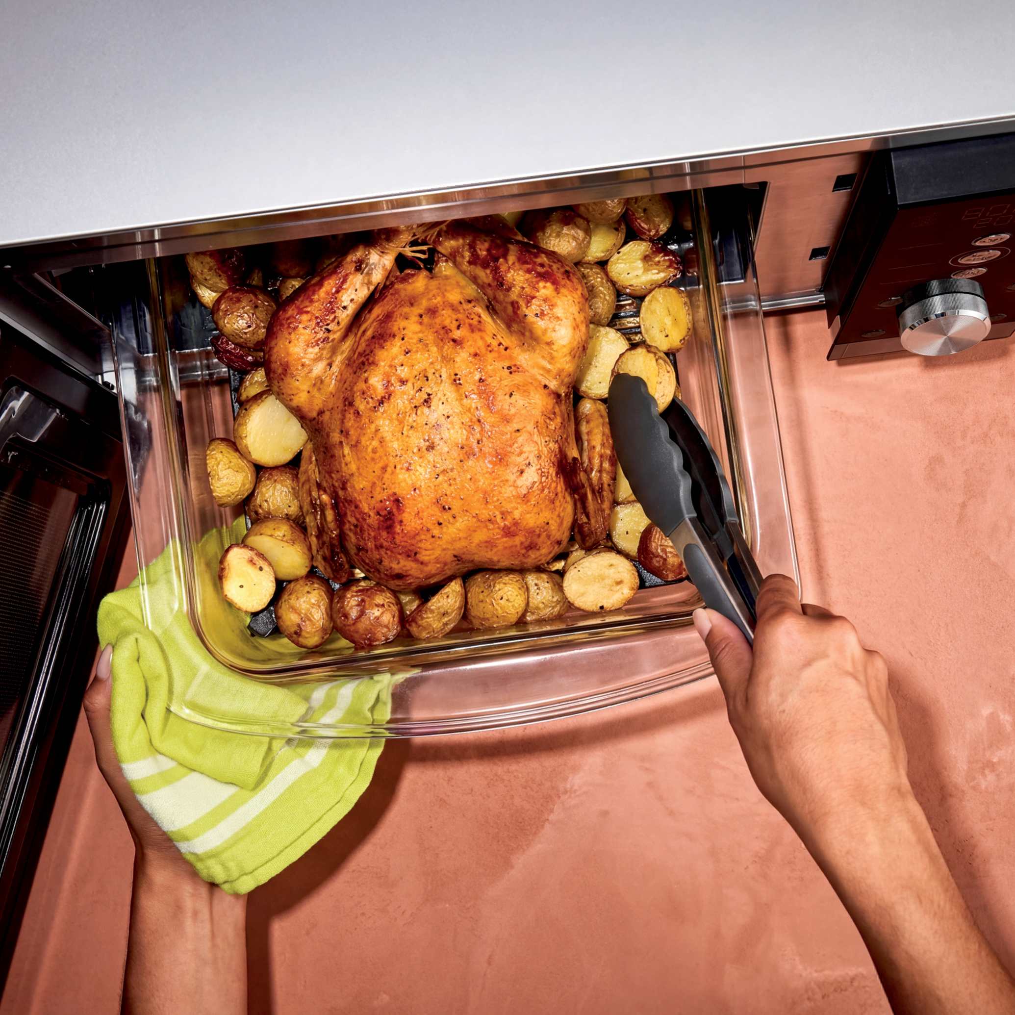 Ninja CRISPi microwave in Silver, overhead lifestyle shot of hands lifting a roast dinner from the open drawer
