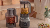 Ninja CrushBOSS in Onyx, food processor and blender jug in use with chickpeas and a salad on the counter