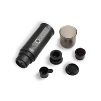 Outin Nano portable espresso machine in Space Grey with ground coffee, coffee capsules and a glass of espresso