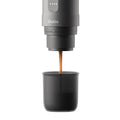 Outin Nano portable espresso machine in Space Grey with ground coffee, coffee capsules and a glass of espresso