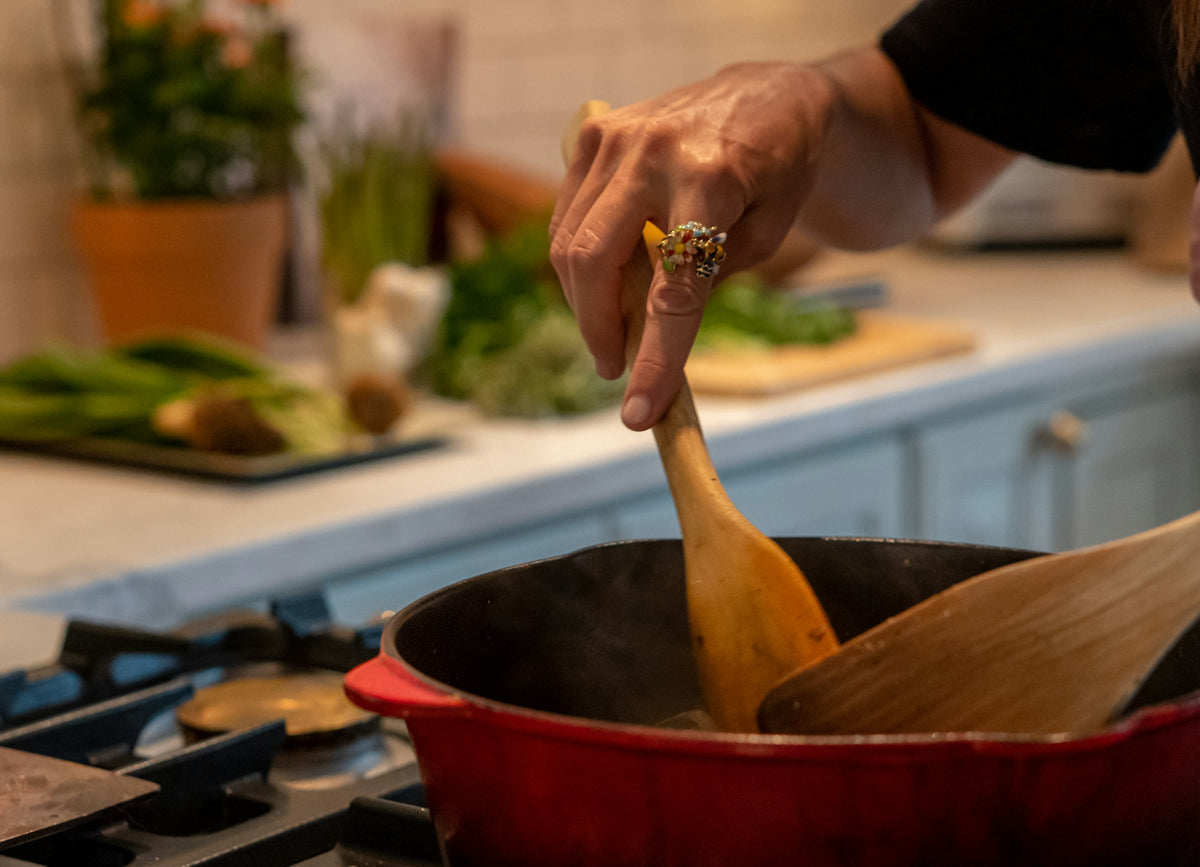 Stirring a red casserole pot on a gas hob with a wooden spoon