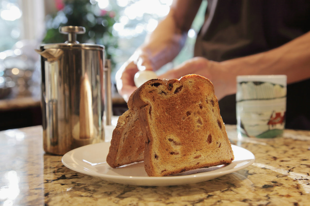 Thick slices of toast on a plate beside a cafetière and a mug on a stone counter