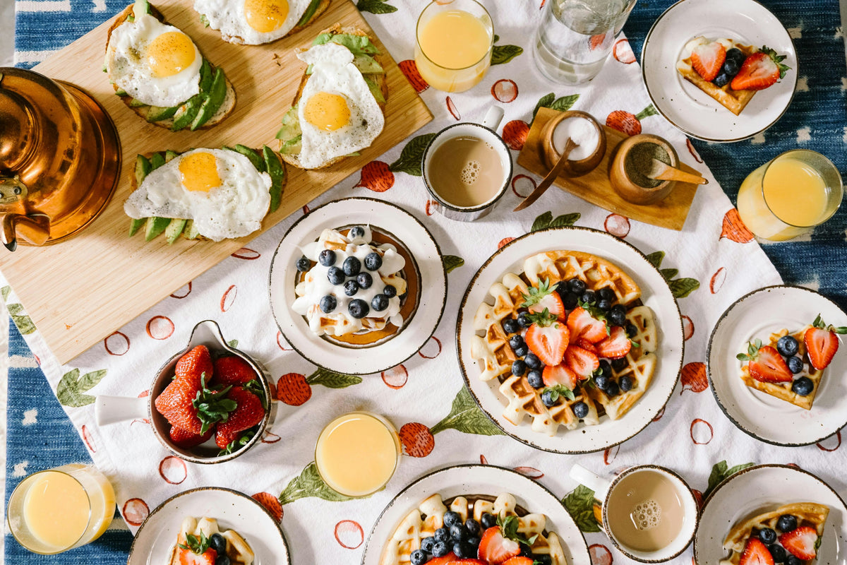 Breakfast table with waffles, berries, fried eggs and glasses of orange juice