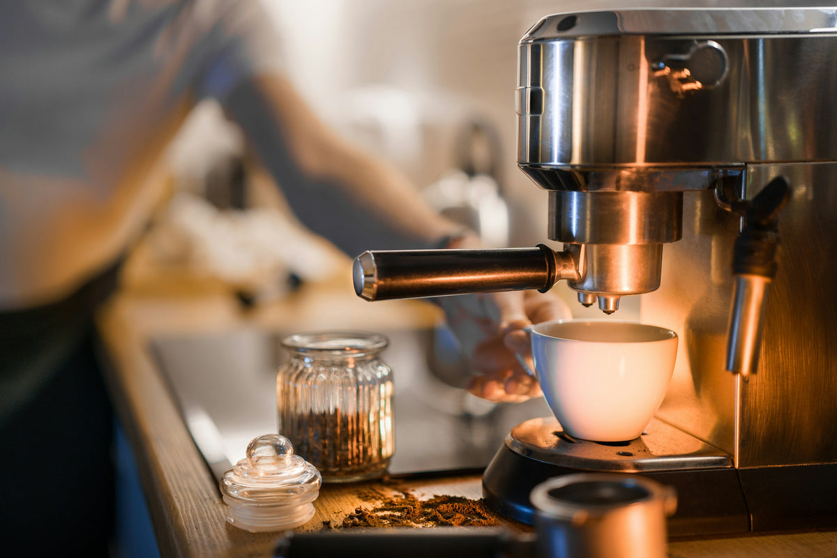 Espresso machine filling a white cup on a kitchen worktop, with a jar of ground coffee beside it