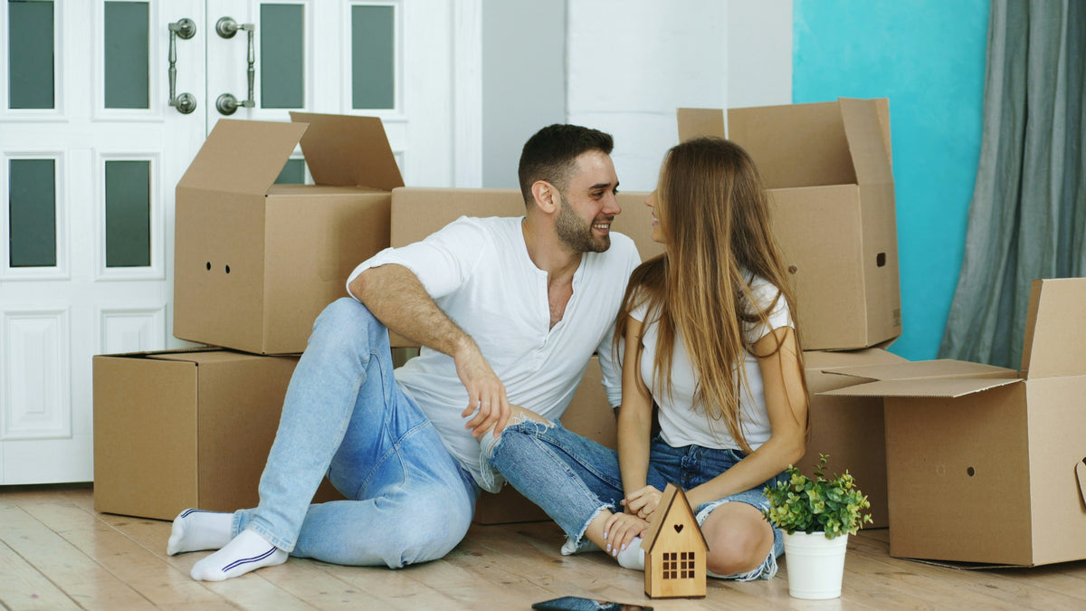 A couple sitting on the floor among cardboard moving boxes in a new home