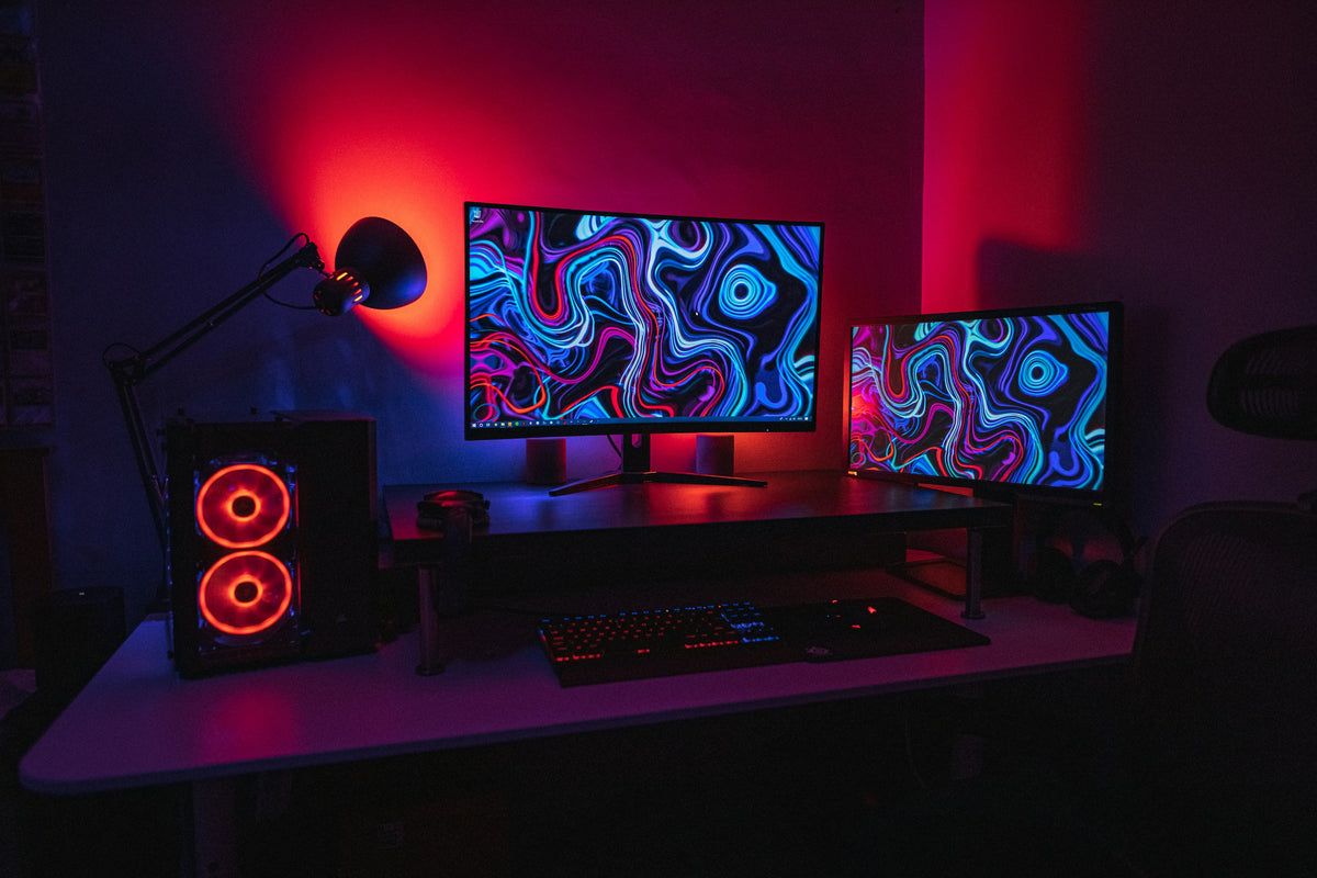 A gaming desk at night with two monitors, a PC with lit fans and a desk lamp