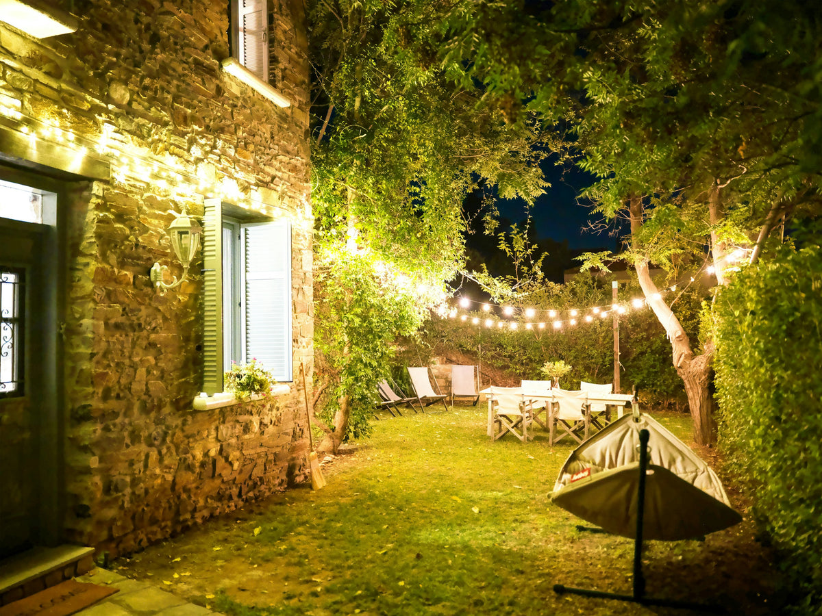 A stone house and garden at night, lit by string lights over a table and chairs
