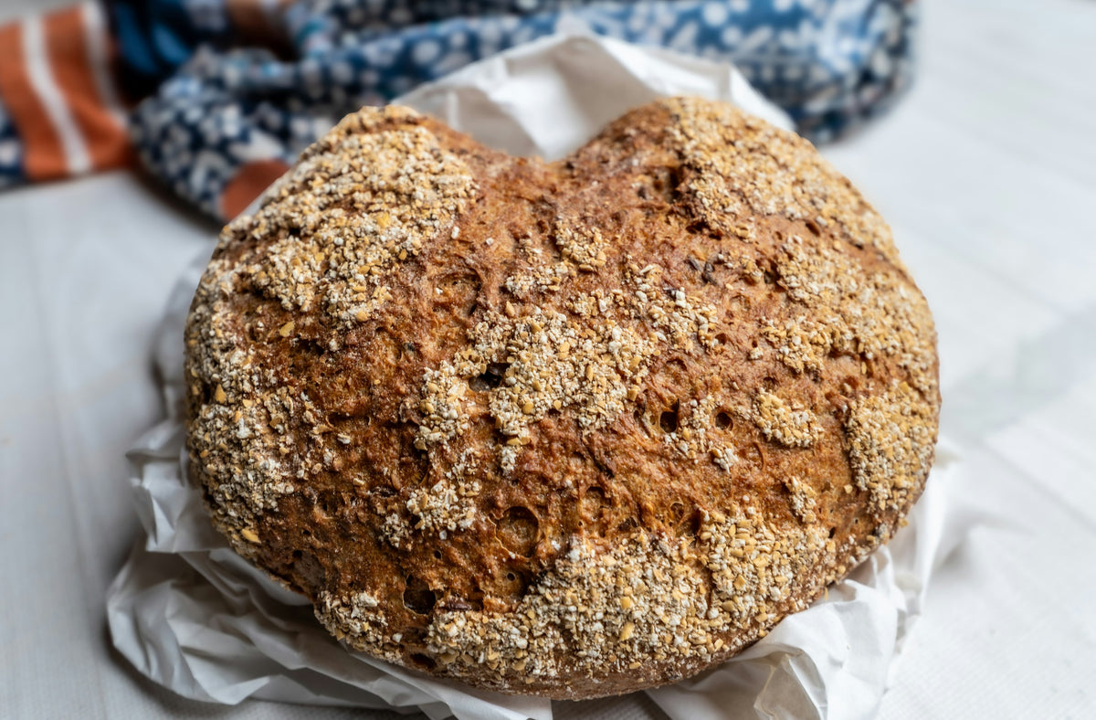 Round loaf of brown bread topped with oats, on baking paper