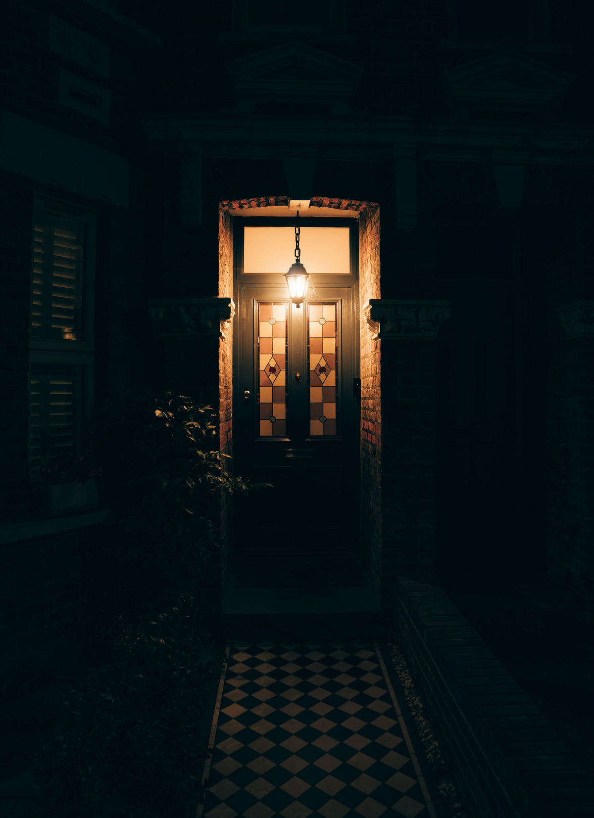 A front door with stained glass panels, lit by a hanging lantern at night
