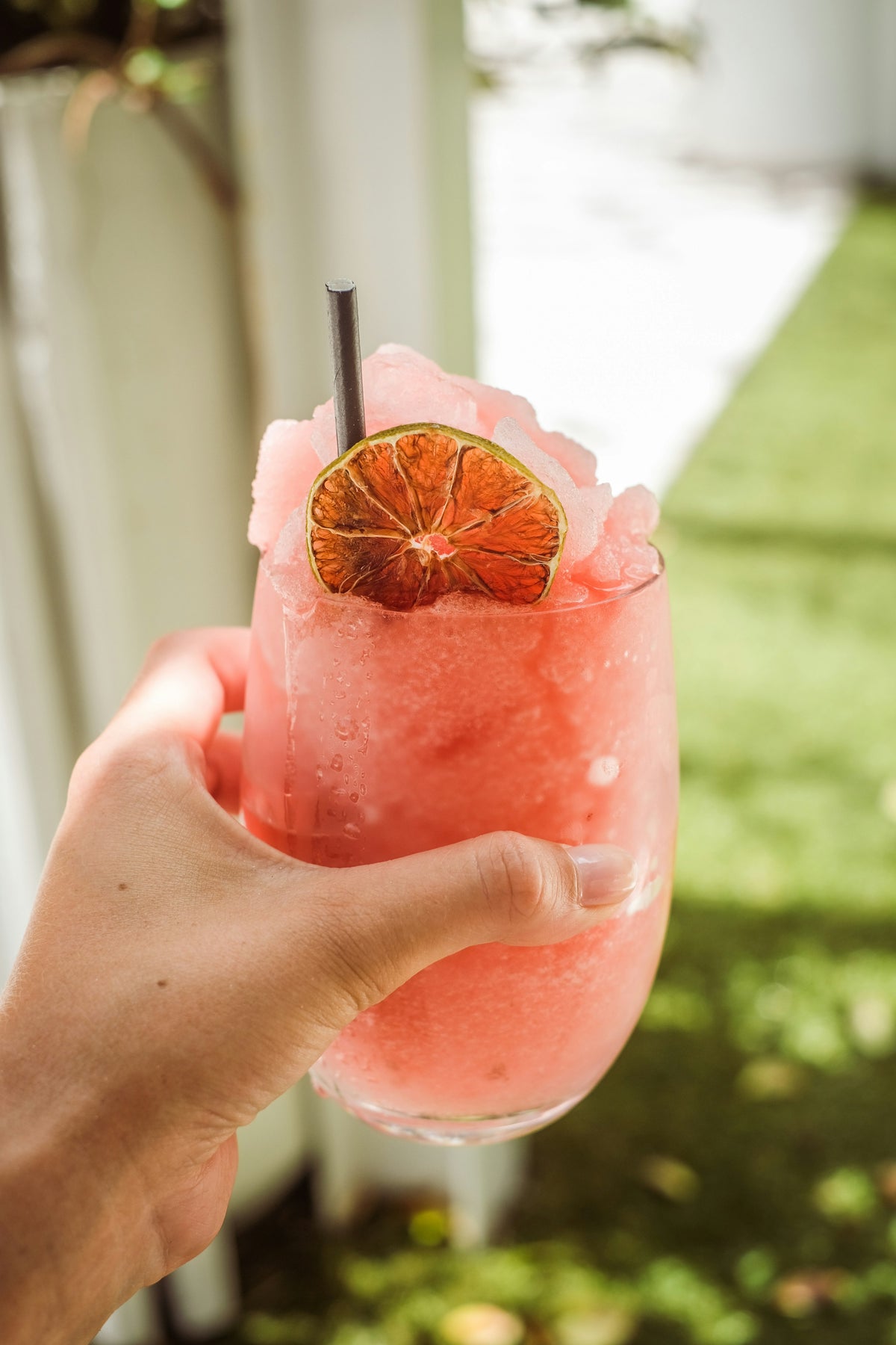 A hand holding a pink frozen drink with a dried lime slice and a straw