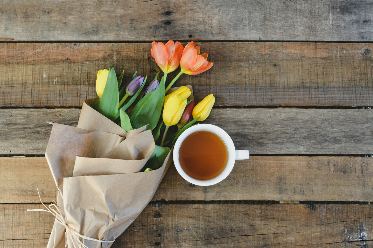 Tulips wrapped in brown paper beside a cup of tea on a wooden table