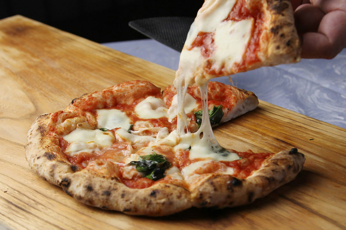 Hand lifting a slice of margherita pizza from a wooden board