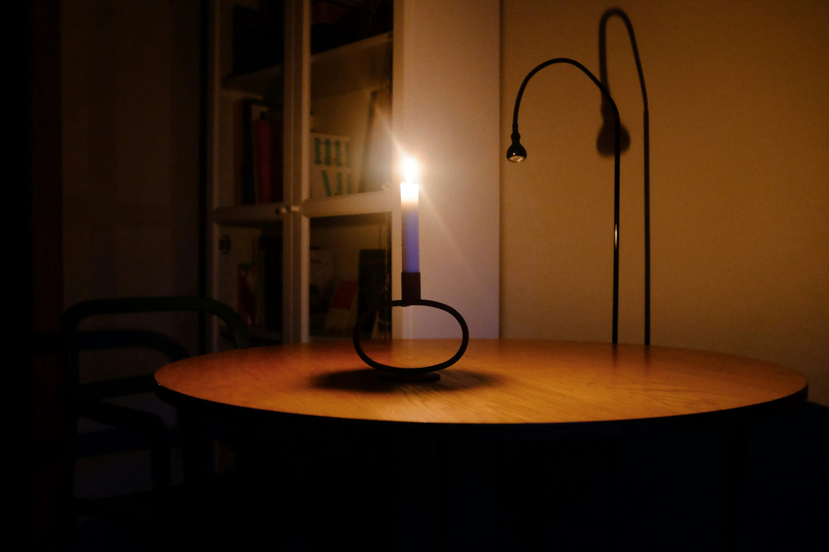A lit candle on a round table in a dark room, with a desk lamp switched off