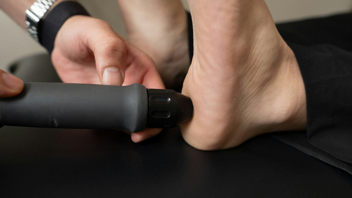 A handheld massager held against the back of a bare heel on a black couch