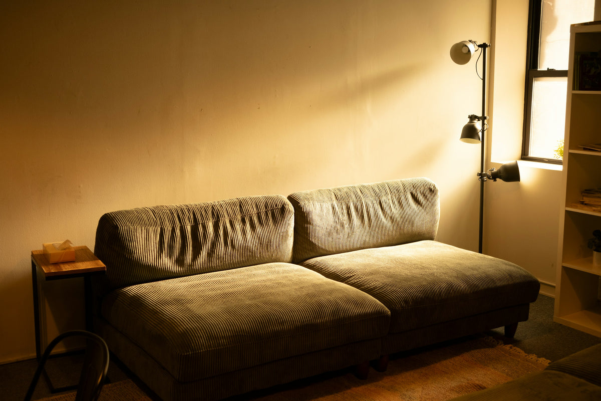 A corduroy sofa in a room lit by a floor lamp and a wall light in the evening