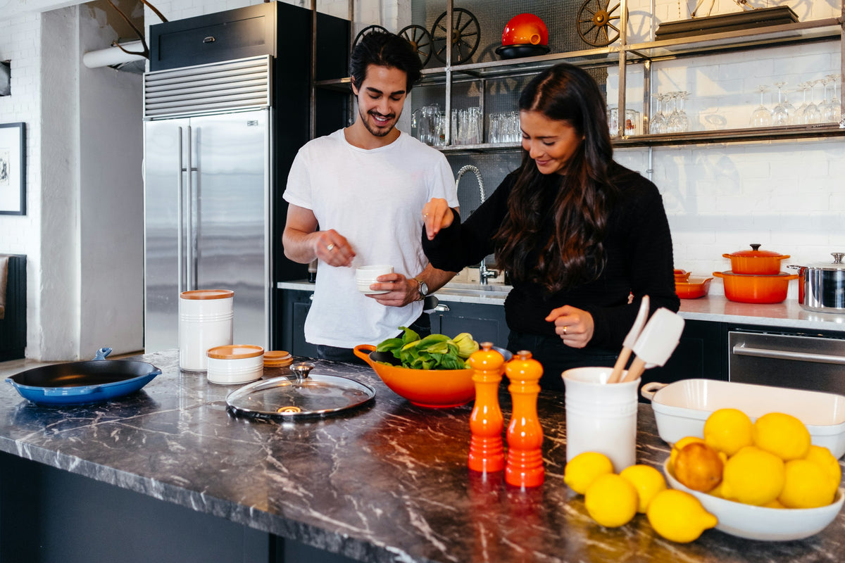 Two people cooking together at a dark marble kitchen counter with a bowl of lemons