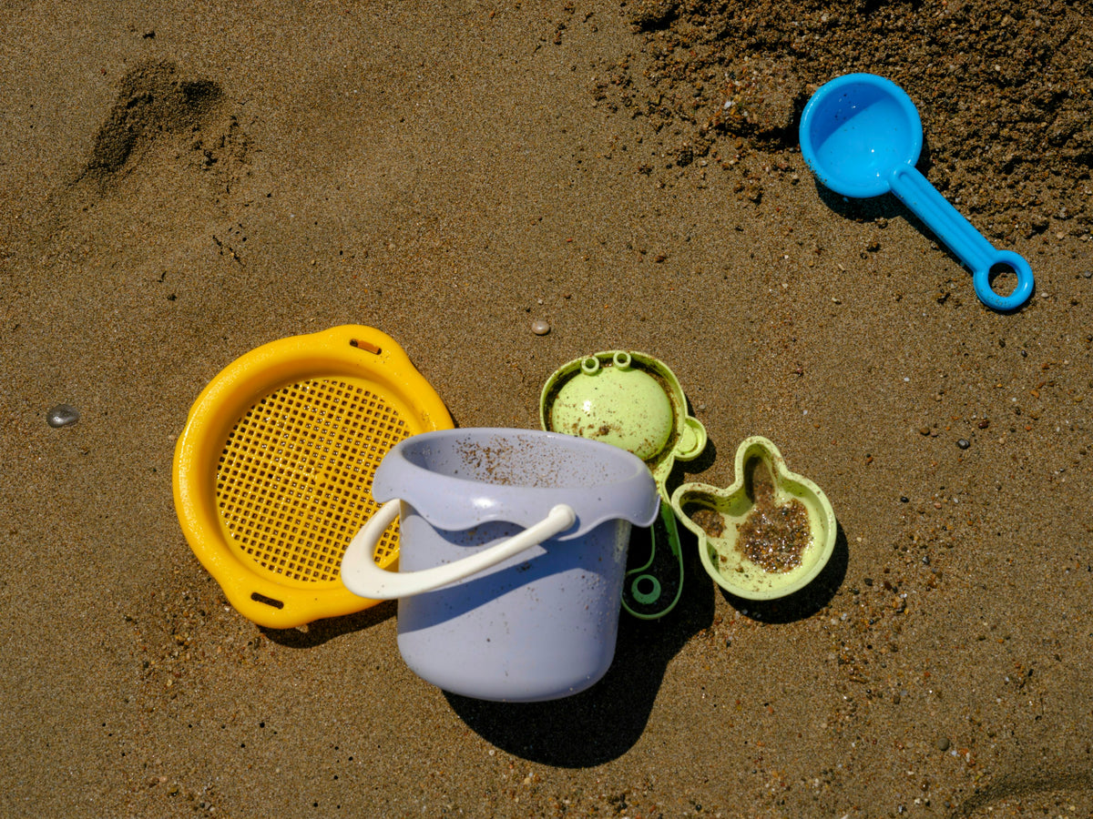 A sand bucket, sieve, moulds and a scoop on wet sand