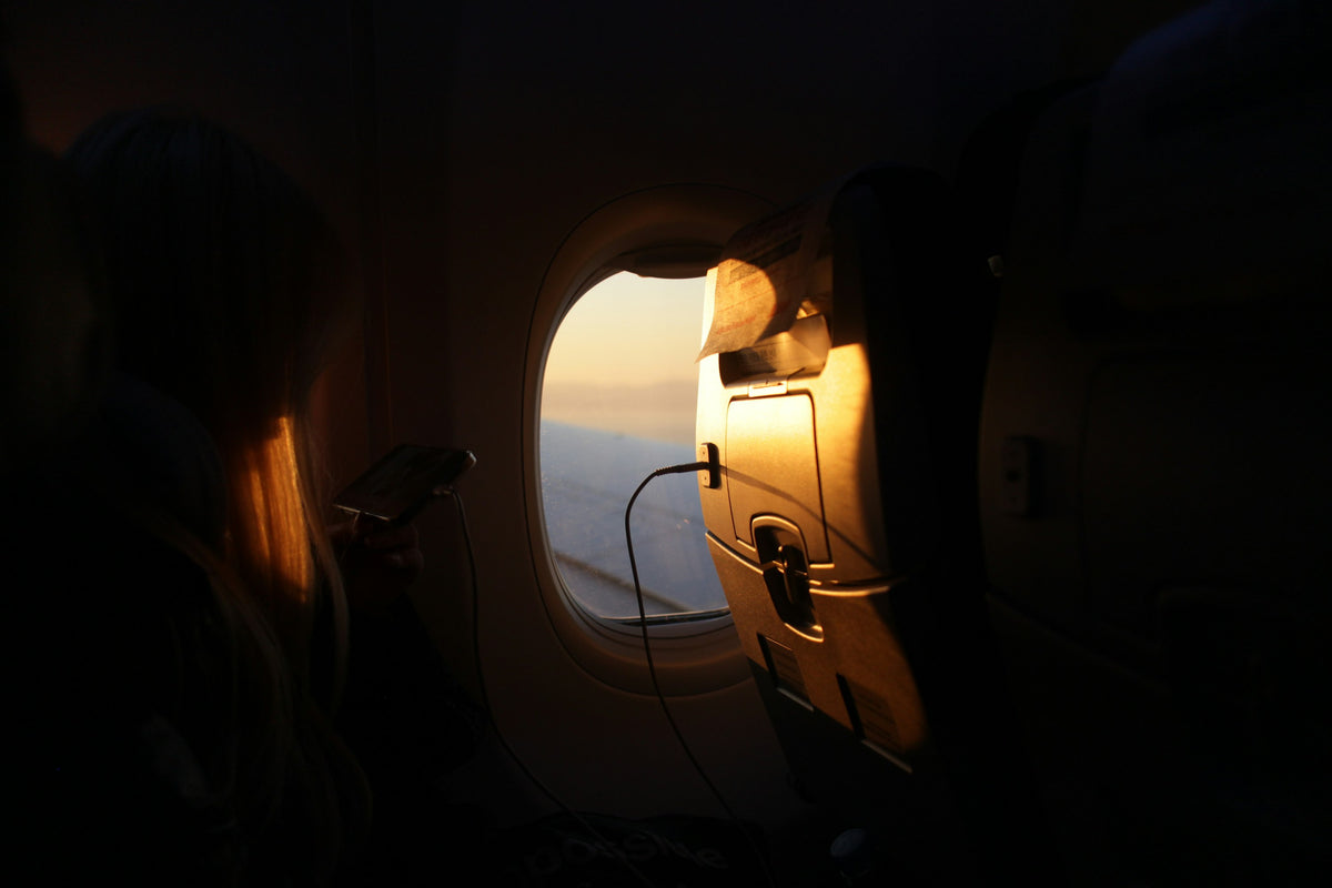 A passenger charges a phone from the seat-back USB port beside an aircraft window at sunrise